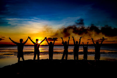 Silhouette people at beach against sky during sunset