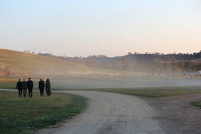 Rear view of people walking on road against sky during sunset