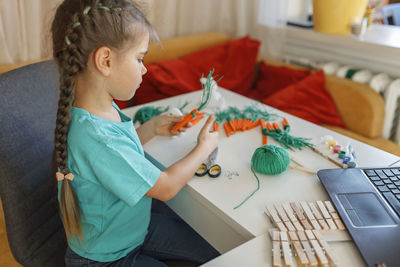 Side view of girl doing craft while watching videos on laptop at home