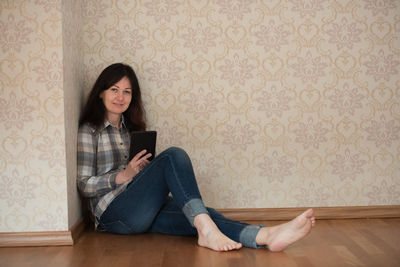Portrait of mature woman using mobile phone while sitting on hardwood floor at home