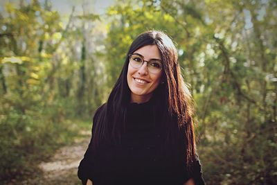 Portrait of smiling young woman standing against trees