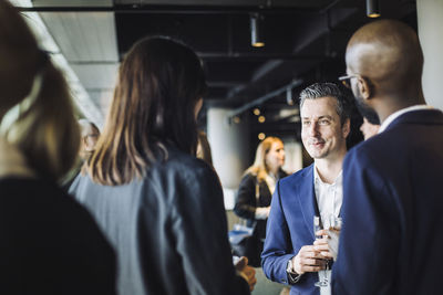 Smiling entrepreneur talking to colleagues while holding drinking glass at workplace