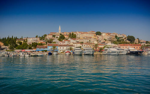 Sailboats in sea by buildings against clear blue sky