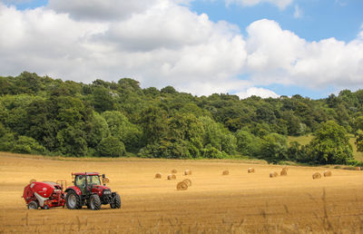 Red tractor by hay bales on field against trees