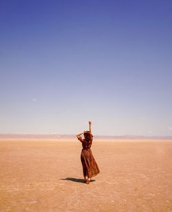 Rear view of carefree woman with arms raised walking on desert against sky during sunny day