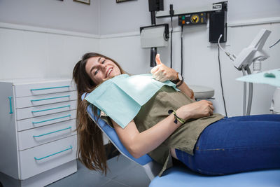 Portrait of smiling young woman showing thumbs up on dentist chair