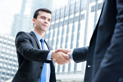 Business people shaking hands while standing against buildings