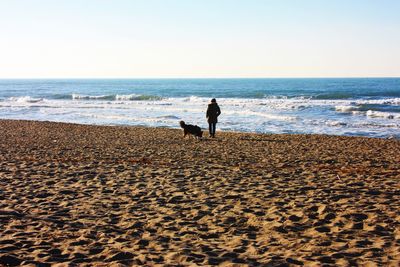 Woman with dog on beach against clear sky