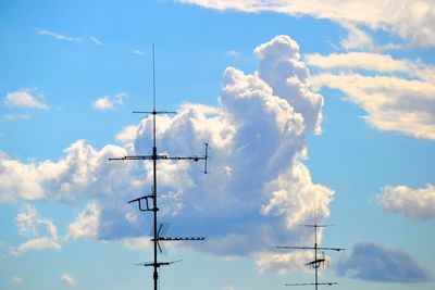 Low angle view of antennas against cloudy sky