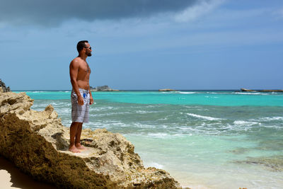 Man standing on rock at beach against sky