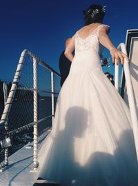 Rear view of bride amidst railing on boat against clear blue sky
