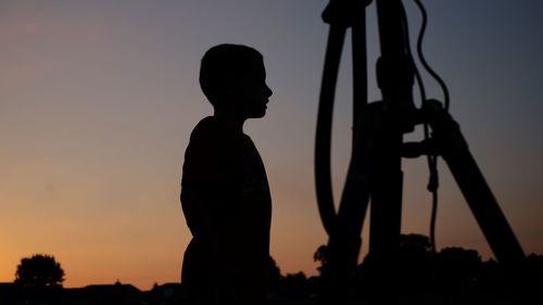 Low angle view of silhouette boy standing by structure against sky during sunset