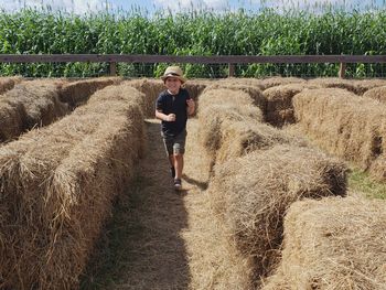 Full length of boy walking amidst hay bales on field