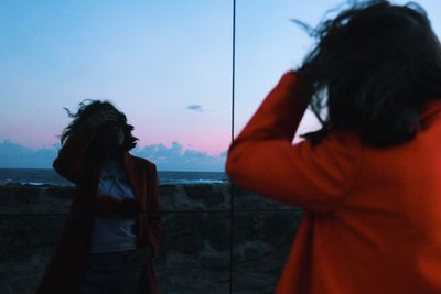 Rear view of young woman standing in front of mirror during sunset