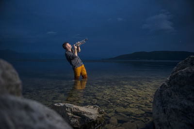 Man standing on rock at beach against sky