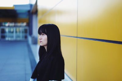 Side view of young woman standing against yellow wall