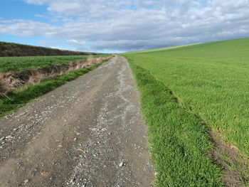 Road passing through field against cloudy sky