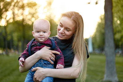 Portrait of cute son carried by mother in park at sunset
