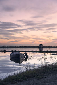 Boat moored on lake against sky during sunset