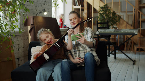 Girl playing guitar by mother at home