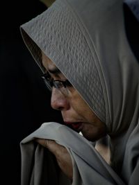 Close-up of mature woman in hijab against black background