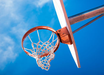 A basketball hoop viewed from a low angle with a beautiful blue sky in the background