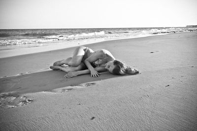 Young woman lying on sand at beach against clear sky