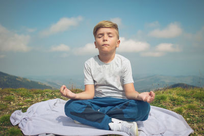 Boy sitting on field against sky