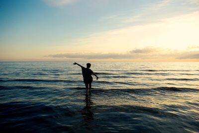 Rear view of woman in sea against sky during sunset