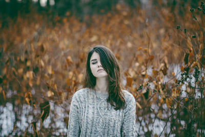 Thoughtful woman wearing sweater standing against dry plants