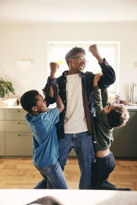 Playful father lifting sons in arms while standing at home