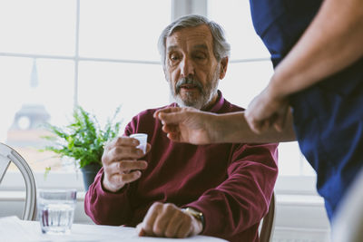 Midsection of caretaker giving medicine to senior man at home