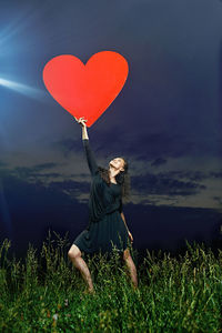 Rear view of woman holding heart shape balloons on field against sky