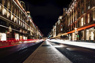 Light trails on city street amidst buildings at night