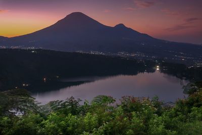 Scenic view of lake by mountains against sky at sunset