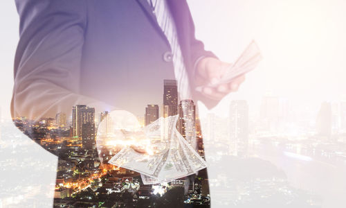 Double exposure of businessman standing against modern illuminated buildings in city