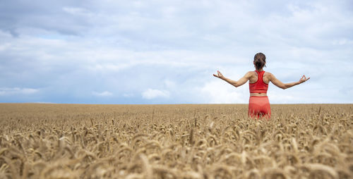 Full length of woman with arms raised standing on field against sky