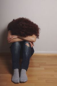 Full length of sad woman sitting on hardwood floor against wall