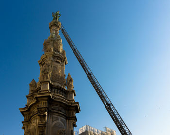 Low angle view of crane by historic building against clear sky