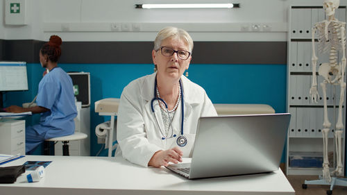 Portrait of doctor with laptop at desk in clinic