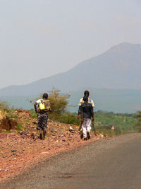 Rear view of men walking on road against mountain range