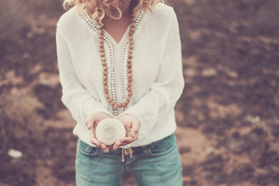 Midsection of woman holding seashell while standing at beach