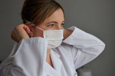 Close-up of thoughtful female doctor wearing mask looking away against gray background