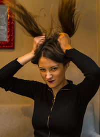 Portrait of frustrated young woman holding pigtails while standing against wall