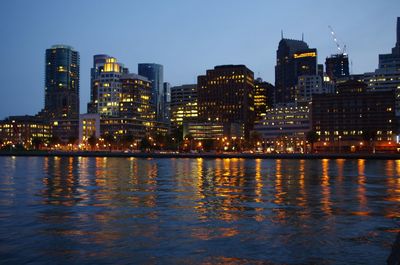 River by illuminated buildings against sky at dusk