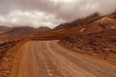 Dirt road on landscape against sky