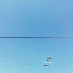 Low angle view of electricity pylon against clear blue sky