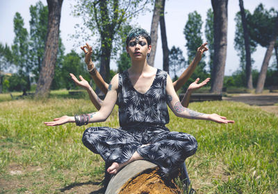 Young woman gesturing mudra while sitting on fallen tree
