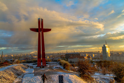 Cross in city against cloudy sky