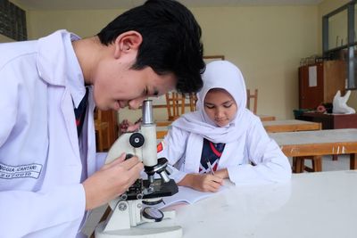 Teenager boy looking through microscope at laboratory